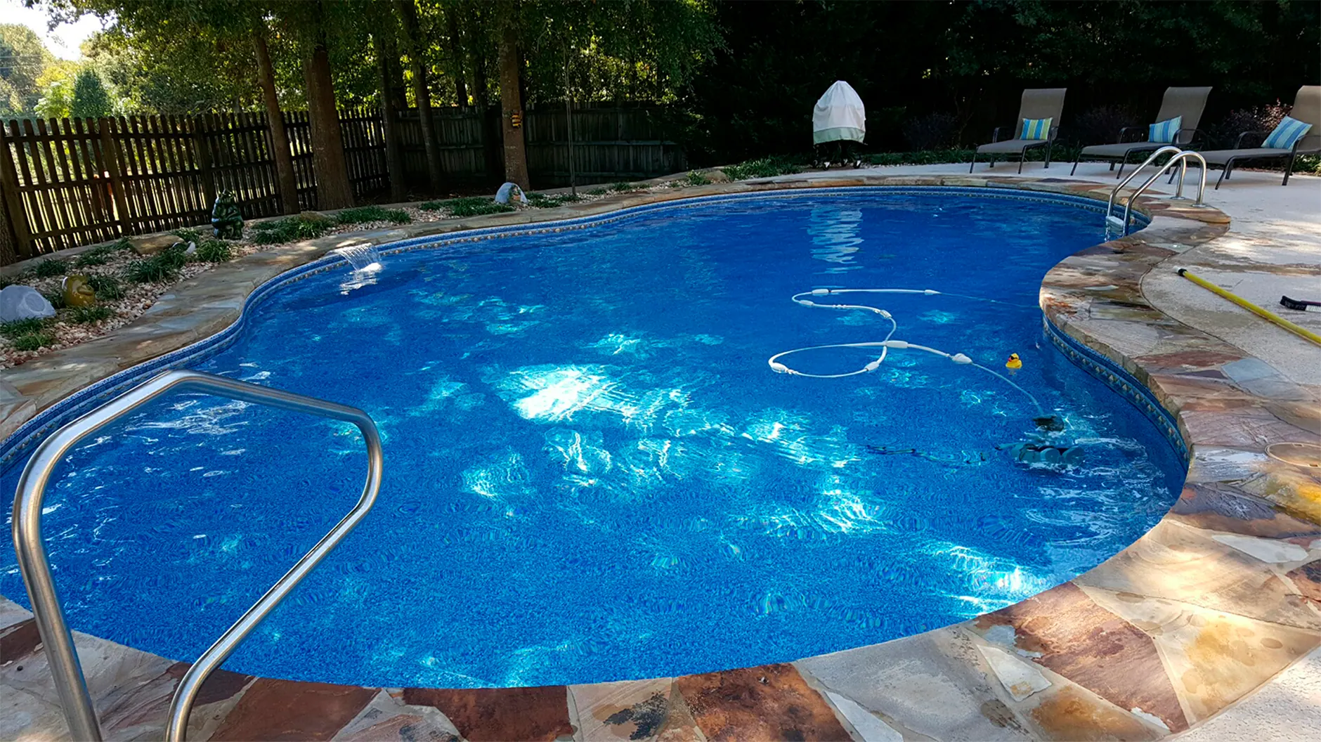 A kidney-shaped backyard pool with flagstone coping, an automatic pool cleaner working along the bottom.