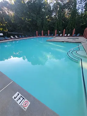 A clear commercial pool at dusk with loungers along the far edge and a 3 FT depth marker on the deck.